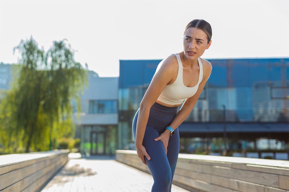 Young woman in athletic wear holding her thigh in discomfort, showing symptoms of radiculopathy in Parsippany-Troy Hills.