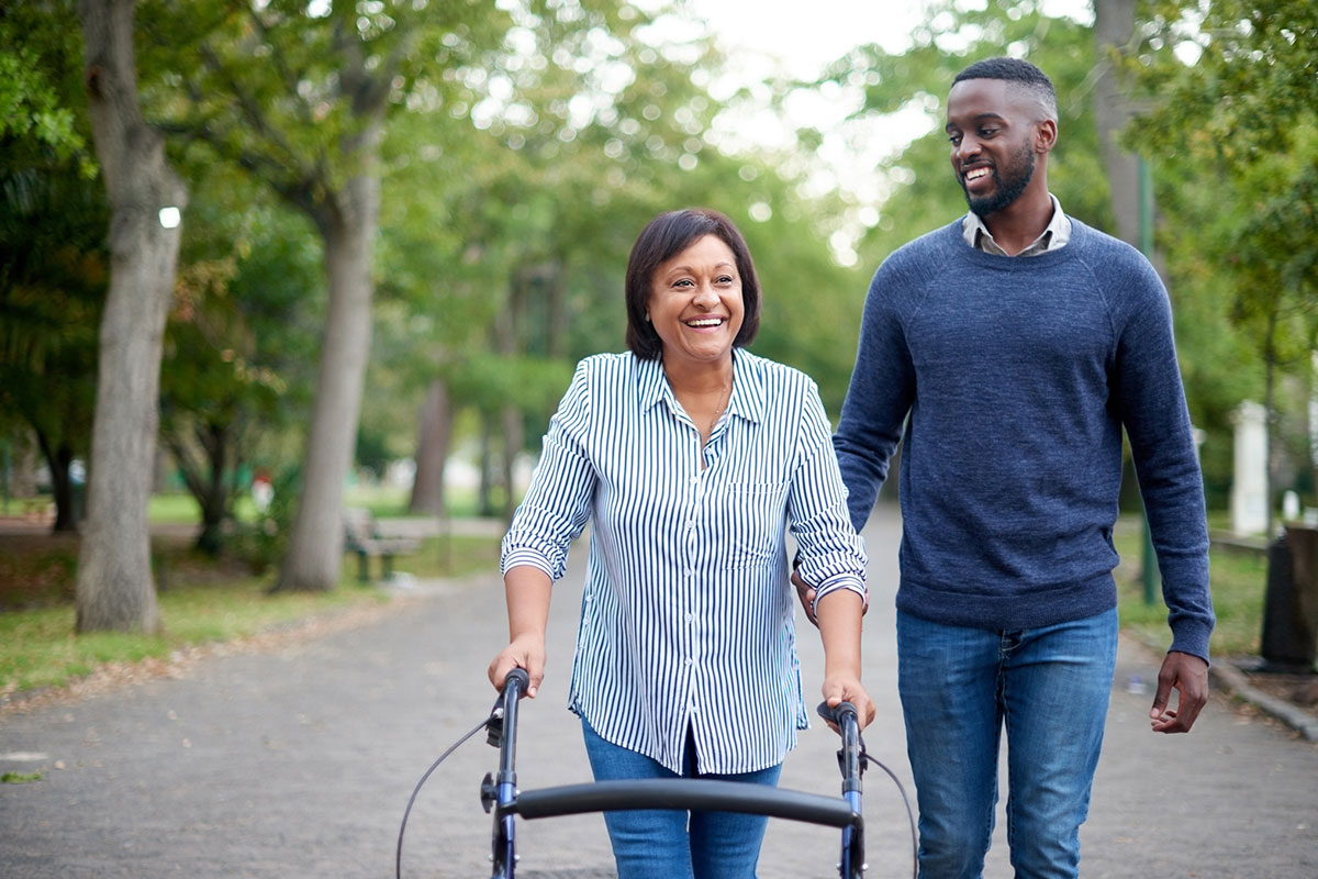 Woman walking outdoors with a mobility aid, smiling alongside a companion after treatment for radiculopathy in Parsippany-Troy Hills.