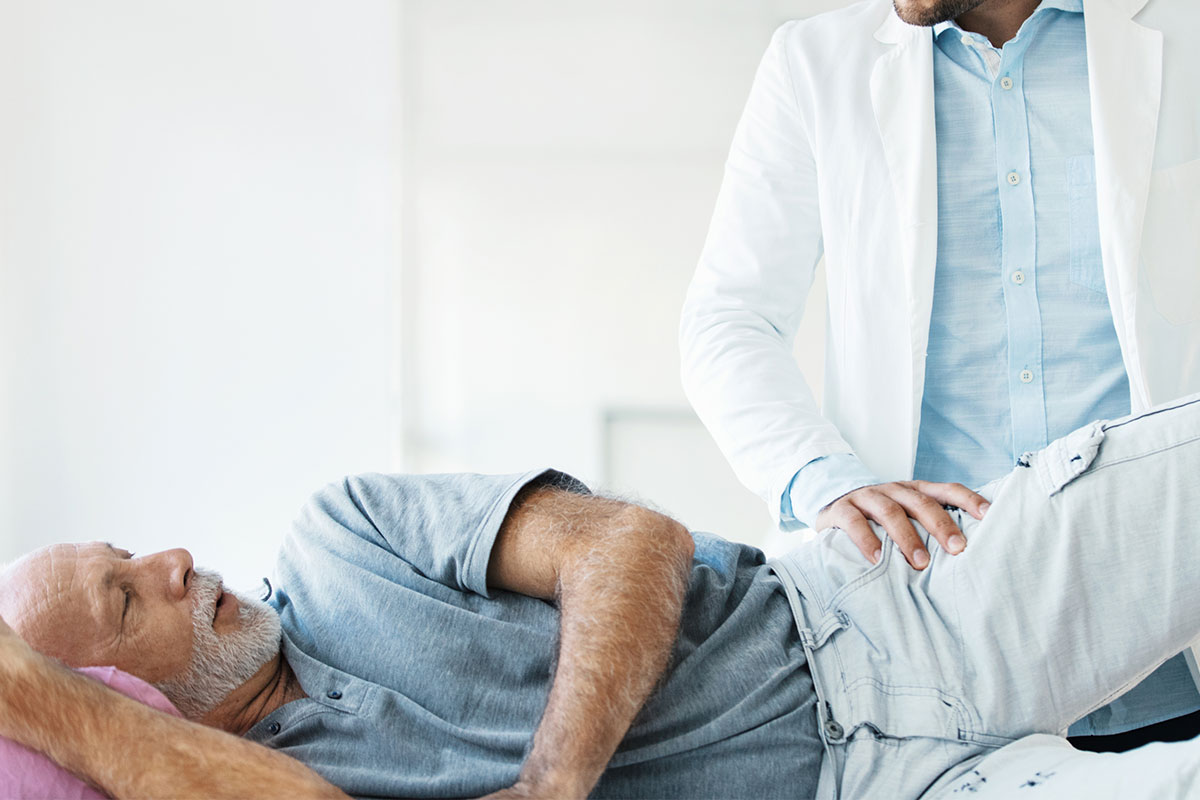 Senior man lying on his side during a physical exam for hip and back pain, preparing for evaluation before sij fusion in Parsippany-Troy Hills