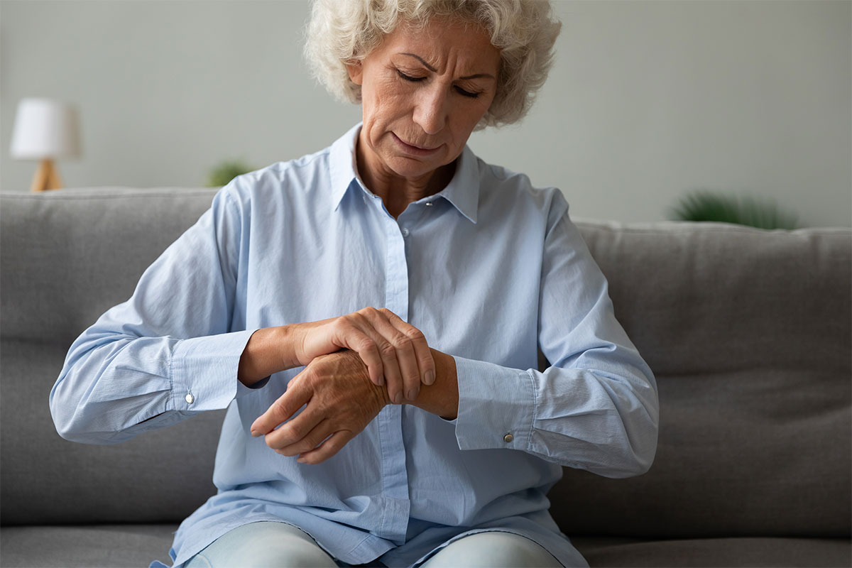Older woman holding her wrist while sitting on a sofa, an example of arthritis relief supported by PRP injections in Parsippany-Troy Hills.